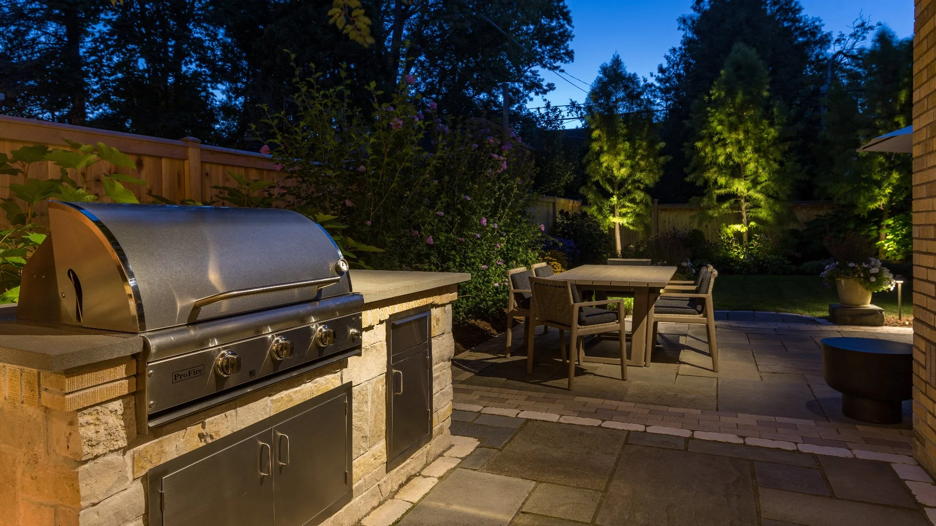 Outdoor kitchen with grill and landscape lighting in a well-maintained backyard in Milwaukee, WI.