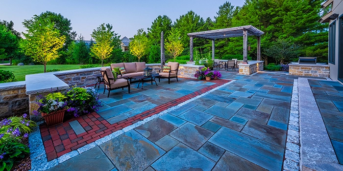 Bright outdoor patio featuring a seating area, stone wall, and pergola surrounded by trees and flowers in Wauwatosa, WI.