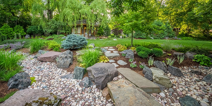 Serene garden featuring a stone path, diverse plants, and large rocks under a canopy of trees in Brookfield, WI.