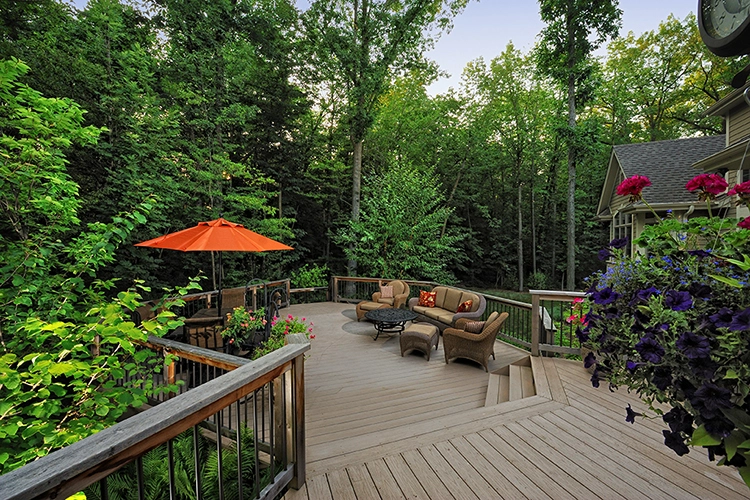 Outdoor deck with wicker seating, an orange umbrella, and colorful flowers, surrounded by trees in Milwaukee, WI.